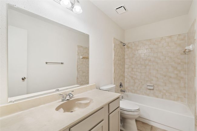 Guest bath with full tub and shower, single vanity, and soft tile accents. | Image 21