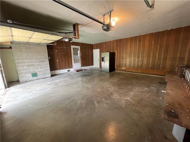 Garage featuring wood walls, a garage door opener, concrete block wall, and stainless steel fridge with ice dispenser | Image 38