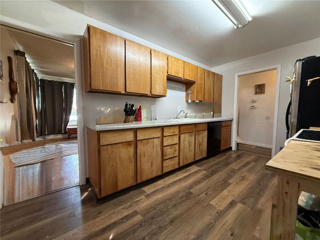 Kitchen with dishwasher, freestanding refrigerator, dark wood-type flooring, light countertops, and brown cabinetry | Image 4