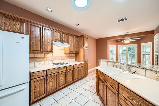 Kitchen featuring white appliances, a sink, under cabinet range hood, backsplash, and light countertops | Image 12