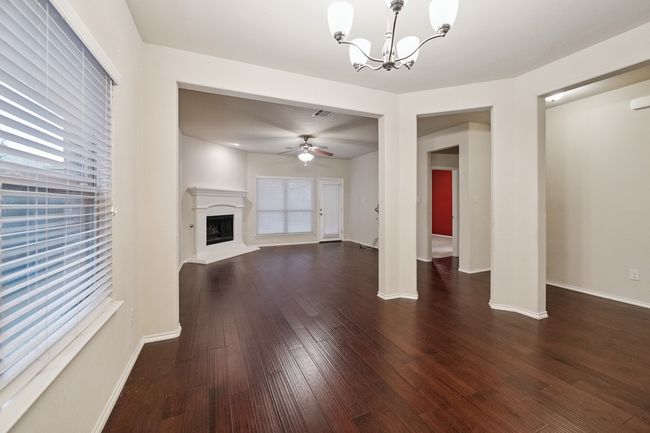 Unfurnished living room with a chandelier, dark wood-style flooring, a fireplace with raised hearth, and ceiling fan | Image 6