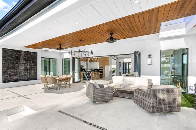 Experience seamless indoor-outdoor living in this elegant covered patio, complete with modern ceiling fans, a cozy sitting area, and a sleek dining space. The open-concept layout connects effortlessly to the kitchen through large folding glass doors, while a stunning stone water feature adds a tranquil touch to this stylish and functional entertaining space. | Image 40
