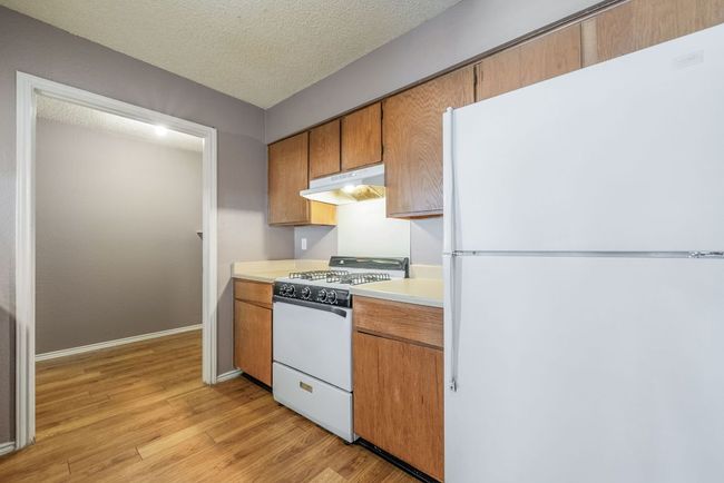 Kitchen featuring white appliances, under cabinet range hood, light wood-style flooring, light countertops, and brown cabinets | Image 14