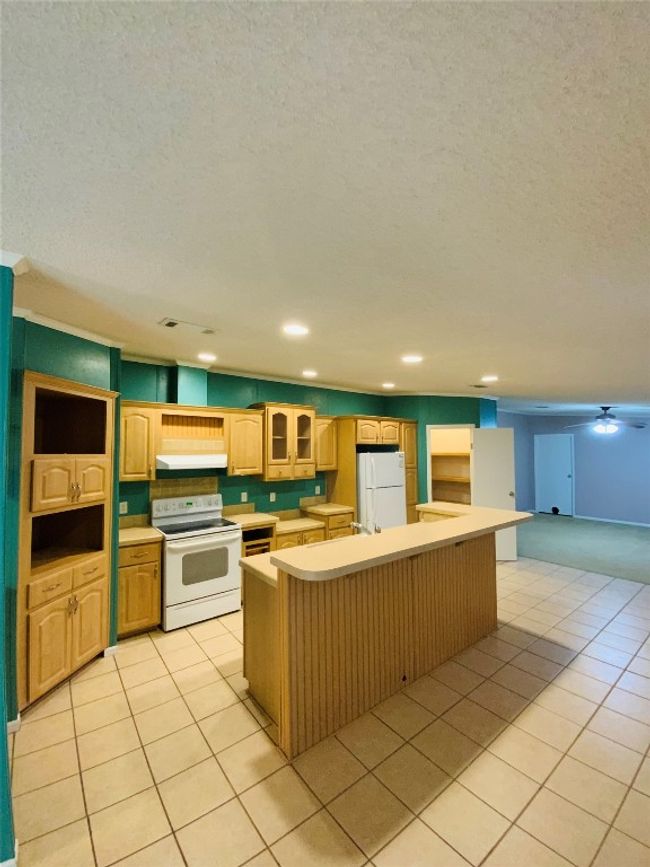 Kitchen with under cabinet range hood, light countertops, light tile patterned floors, white appliances, and a center island with sink | Image 6