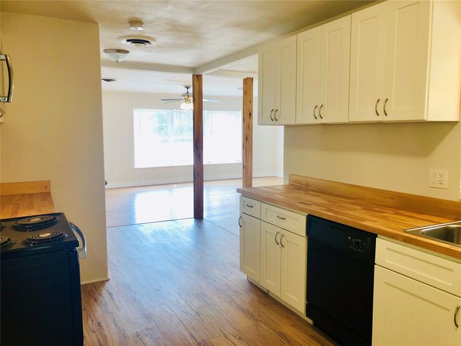Kitchen with butcher block counters, black appliances, light wood-type flooring, ceiling fan, and white cabinets | Image 6