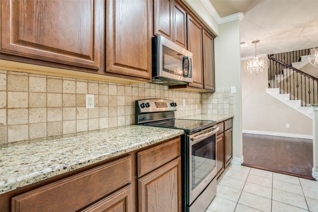 Kitchen with stainless steel appliances, ornamental molding, light stone counters, light tile patterned floors, and a chandelier | Image 5
