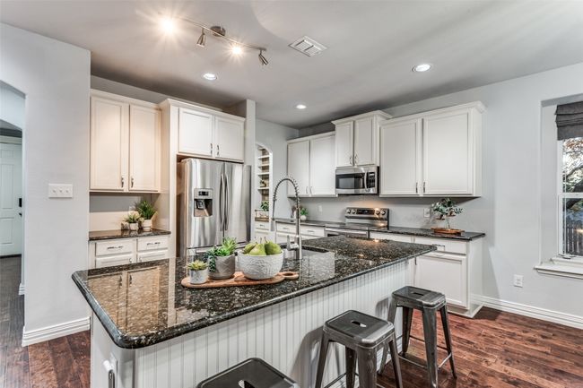 Kitchen featuring stainless steel appliances, a center island with sink, a kitchen bar, dark wood-style flooring, and dark stone counters | Image 18