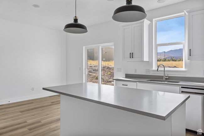 Kitchen featuring light wood finished floors, a sink, pendant lighting, stainless steel dishwasher, and white cabinets | Image 9
