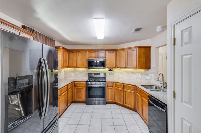 Kitchen featuring visible vents, brown cabinets, a sink, tasteful backsplash, and stainless steel appliances | Image 11