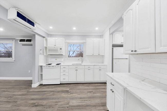 Kitchen with white appliances, an AC wall unit, a sink, decorative backsplash, and recessed lighting | Image 8