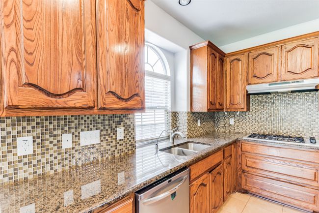Kitchen with dishwasher, under cabinet range hood, gas stovetop, stone countertops, and brown cabinets | Image 13