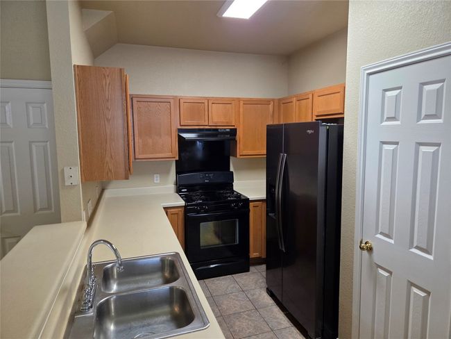 Kitchen with black appliances, light countertops, light tile patterned floors, and under cabinet range hood | Image 12