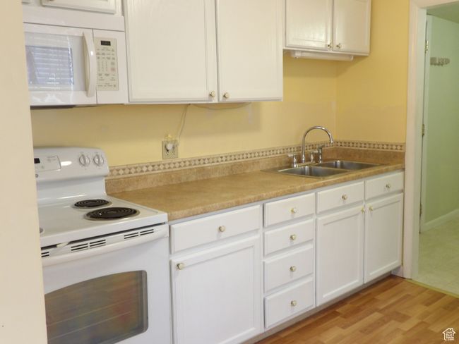 Kitchen with white appliances, sink, white cabinets and light laminate flooring. | Image 18