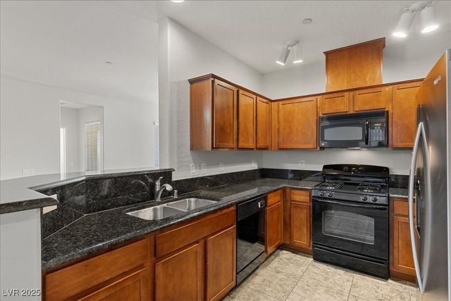 Kitchen with black appliances, dark stone counters, light tile patterned floors, and brown cabinetry | Image 7