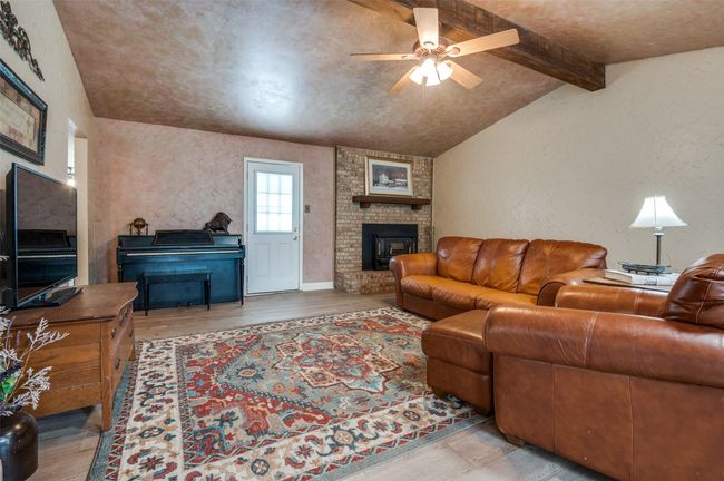 Living room with a textured wall, lofted ceiling with beams, a fireplace, a ceiling fan, and wood finished floors | Image 7