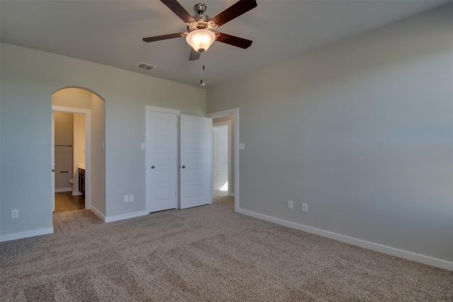 Unfurnished bedroom featuring arched walkways, carpet flooring, baseboards, ensuite bath, and ceiling fan | Image 9