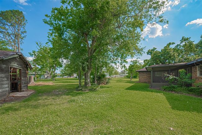 This photo showcases a spacious backyard with lush greenery, mature oak and pecan trees, and a charming rustic outbuilding. The main house features a screened porch, perfect for enjoying the outdoor space. Ideal for those seeking a serene and natural setting. | Image 29