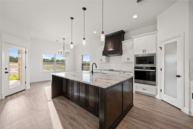 Kitchen with oven, custom exhaust hood, stainless steel microwave, a sink, and light wood-style flooring | Image 15
