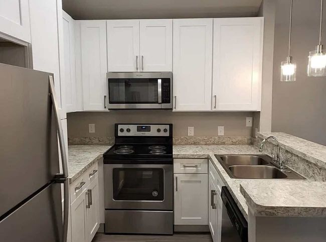 Kitchen with stainless steel appliances, a sink, light countertops, white cabinetry, and a peninsula | Image 6