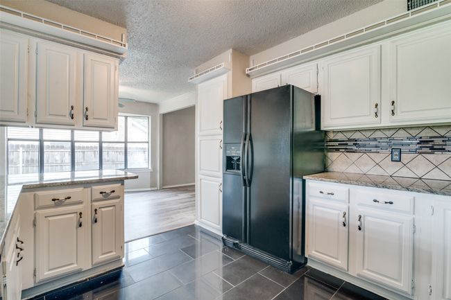 Kitchen with black refrigerator with ice dispenser, white cabinets, dark tile patterned flooring, and a textured ceiling | Image 11