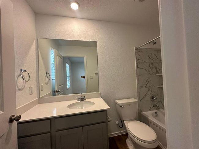Bathroom featuring a textured wall, toilet, vanity, shower / bathtub combination, and wood finished floors | Image 13