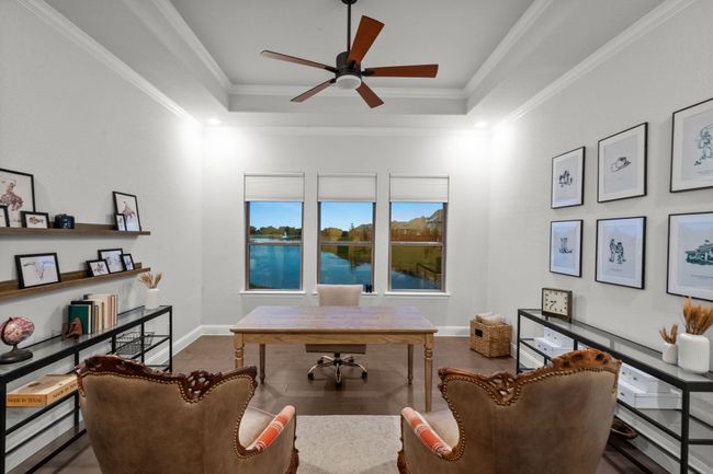 Dedicated office space with a tray ceiling, wood floors, water views, a ceiling fan, and crown molding | Image 24