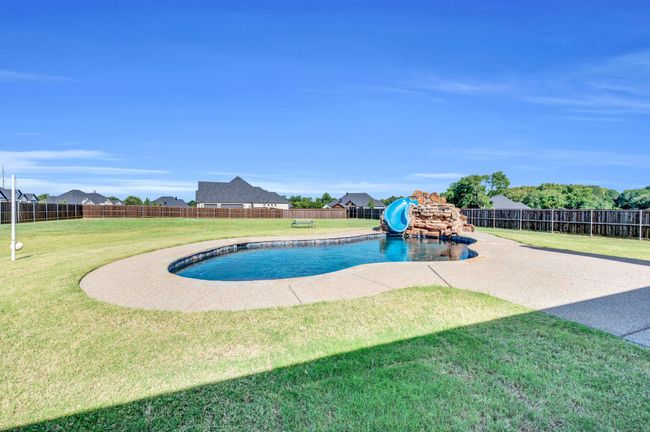 View of swimming pool featuring a water slide, a fenced backyard, and a residential view | Image 4