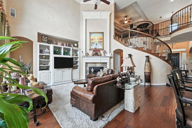 Living room featuring a ceiling fan, a towering ceiling, stairway, a tiled fireplace, and dark wood-type flooring | Image 10