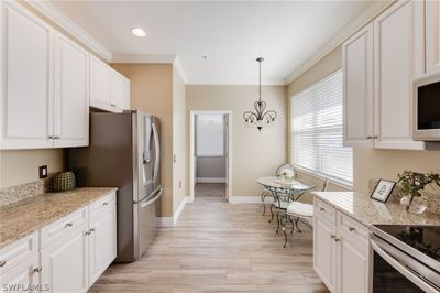 Kitchen with white cabinetry, hanging light fixtures, ornamental molding, light hardwood / wood-style floors, and stainless steel appliances | Image 3