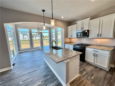 Kitchen with dark wood-type flooring, sink, decorative light fixtures, black appliances, and white cabinetry | Image 3