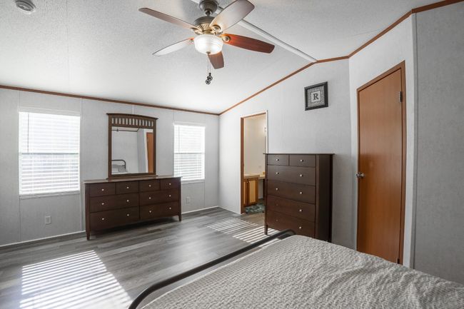 Bedroom with lofted ceiling, wood finished floors, ceiling fan, ornamental molding, and connected bathroom | Image 18