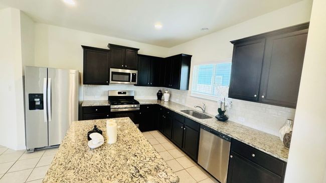 Kitchen featuring stainless steel appliances, decorative backsplash, light tile patterned floors, light stone countertops, and dark cabinetry | Image 20