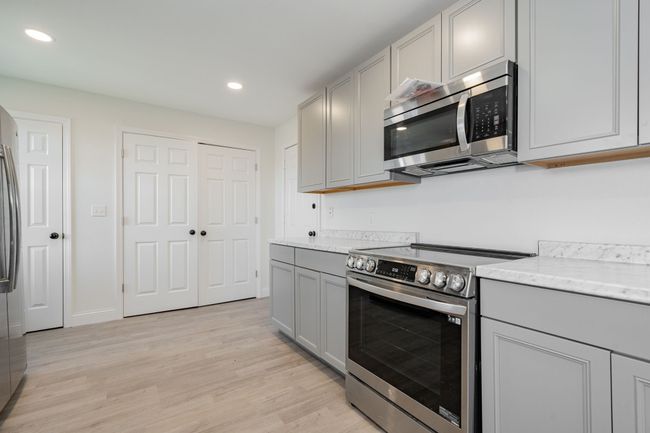 Kitchen featuring stainless steel appliances, gray cabinetry, recessed lighting, light wood-type flooring, and light stone counters | Image 10