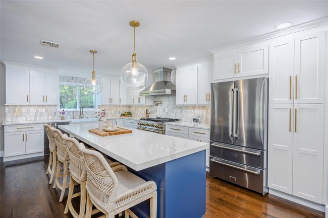 Kitchen with high end appliances, wall chimney range hood, white cabinets, dark wood-type flooring, and a breakfast bar | Image 5