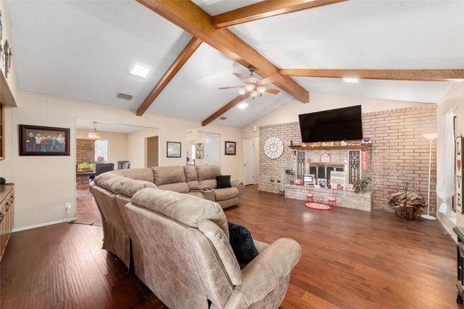 Living room featuring vaulted ceiling with beams, a brick fireplace, dark hardwood / wood-style flooring, brick wall, and ceiling fan with notable chandelier | Image 6