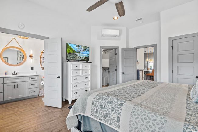Bedroom featuring light wood finished floors, an AC wall unit, connected bathroom, and visible vents | Image 16