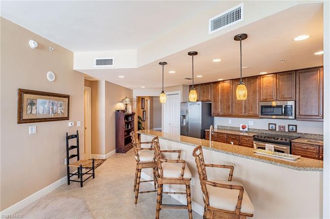 Kitchen with light tile patterned flooring, hanging light fixtures, light stone countertops, appliances with stainless steel finishes, and a kitchen breakfast bar | Image 12
