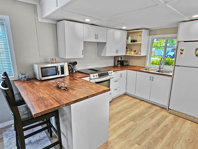 Kitchen featuring a peninsula, a sink, wooden counters, appliances with stainless steel finishes, and light wood finished floors | Image 5