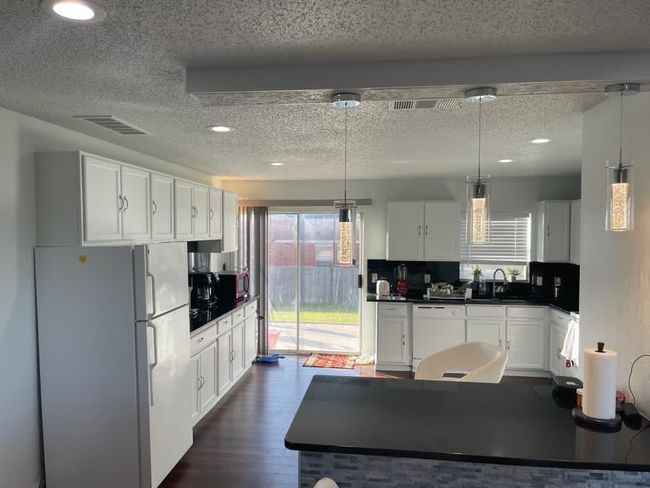Kitchen with white appliances, a textured ceiling, dark countertops, white cabinetry, and recessed lighting | Image 4