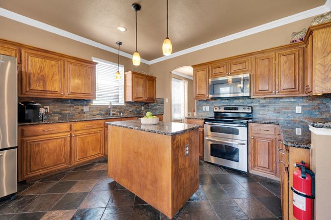 Kitchen with appliances with stainless steel finishes, a center island, brown cabinetry, tasteful backsplash, and dark stone counters | Image 15