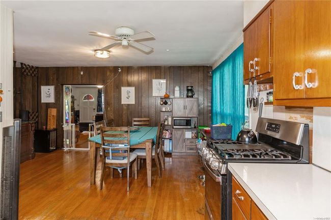 Kitchen featuring stainless steel appliances, wood finished floors, brown cabinets, ceiling fan, and wooden walls | Image 16
