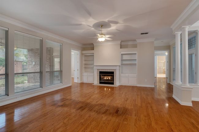 Unfurnished living room featuring decorative columns, a ceiling fan, light wood-style flooring, a tile fireplace, and ornamental molding | Image 4
