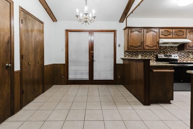 Kitchen with beamed ceiling, stainless steel electric stove, wainscoting, under cabinet range hood, and a notable chandelier | Image 11