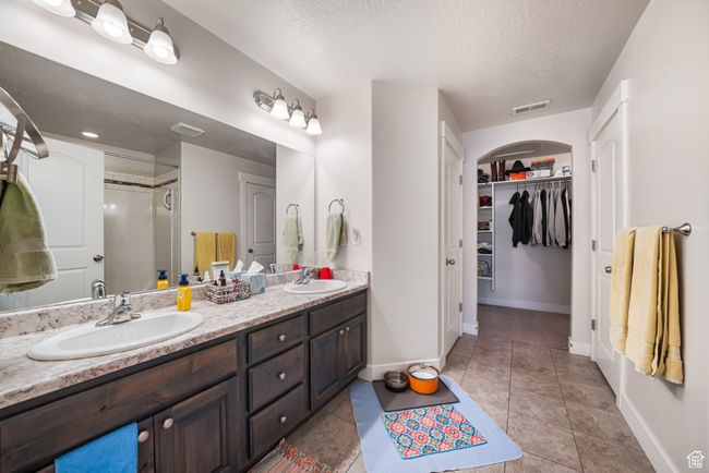 Full bathroom featuring double vanity, a textured ceiling, a spacious closet, a shower, and tile patterned flooring | Image 16