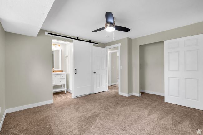Unfurnished bedroom featuring carpet floors, baseboards, a ceiling fan, and a barn door | Image 11