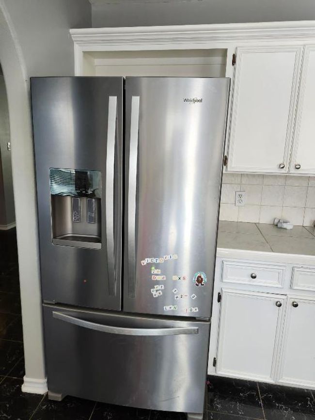 Kitchen view of stainless steel fridge, arched walkways, white cabinets, light countertops, and decorative backsplash | Image 4