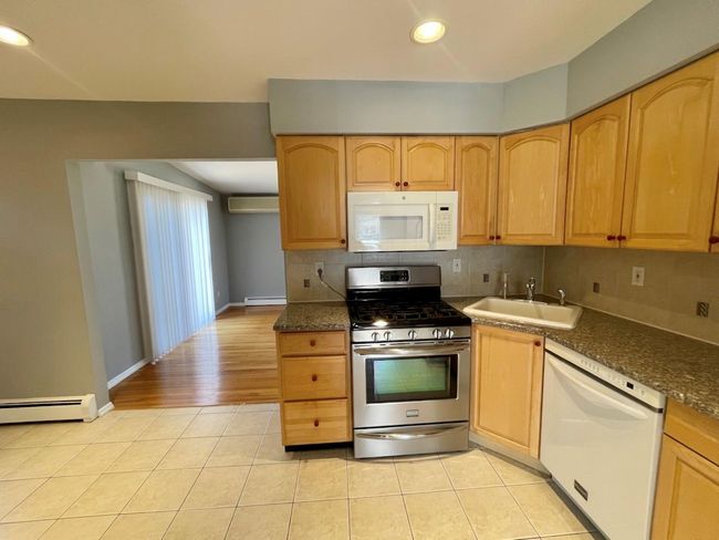 Kitchen with light brown cabinetry, light tile patterned flooring, a sink, and white appliances | Image 4