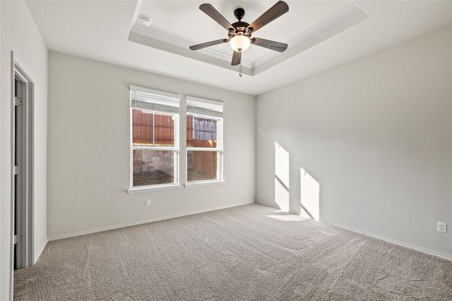 Primary room with ceiling fan, crown molding, a tray ceiling, and light carpet | Image 21