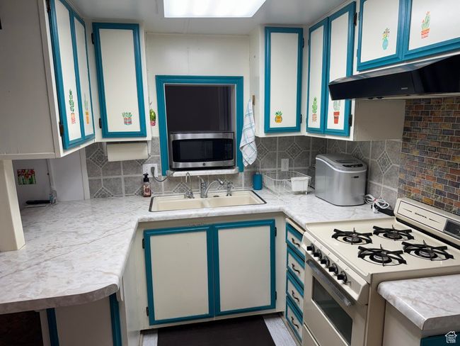 Kitchen with white gas range oven, stainless steel microwave, light countertops, decorative backsplash, and blue cabinets | Image 10