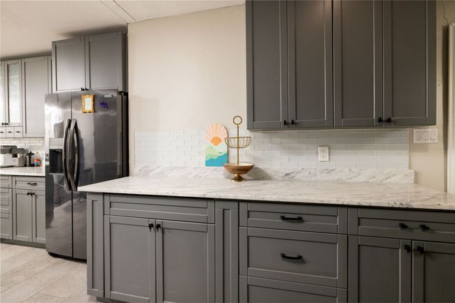 Kitchen with tasteful backsplash, stainless steel fridge, light wood-type flooring, gray cabinetry, and light stone countertops | Image 15